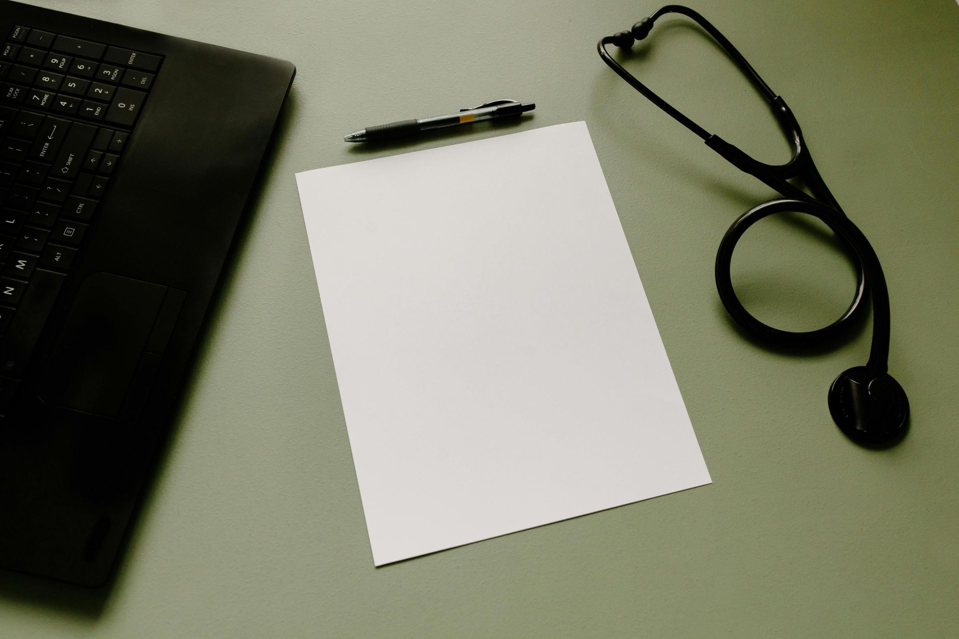 Professional workspace featuring a laptop, stethoscope, pen, and paper sheet for healthcare tasks.